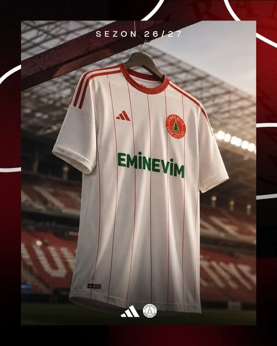 Askıda gösterilen beyaz Ümraniyespor forması; ince kırmızı çizgiler, kırmızı yaka ve yeşil ön sponsor baskısı.